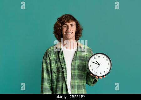 Effektives Zeitmanagement. Glückliche Student hält Uhr auf türkisfarbenem Hintergrund Stockfoto