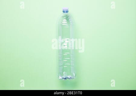 Eine minimalistische leere Plastikflasche, in der Mitte des Bildes, vor einem pastellgrünen Hintergrund, flaches Lay, Studioaufnahme Stockfoto