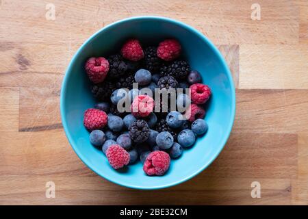 Eine schöne hellblaue Obstschale mit Himbeeren, Heidelbeeren und Brombeeren auf Holzhackbrett, Draufsicht, Studioaufnahme Stockfoto