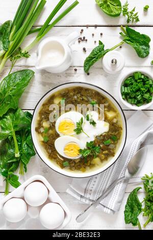 Grüne Sauerampfer- und Spinatsuppe mit gekochtem Ei und saurer Sahne auf weißem rustikalem Holztisch, Draufsicht Stockfoto