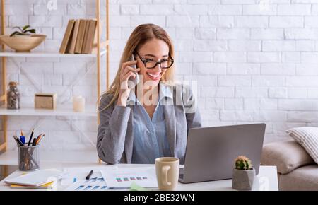 Geschäftsfrau, die am Telefon spricht und sich einen Laptop anschaut Stockfoto