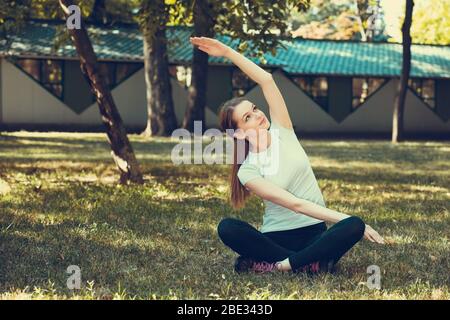 Schöne junge Frau tun Dehnung Übung auf grünem Gras im Park. Yoga-Workout. Stockfoto