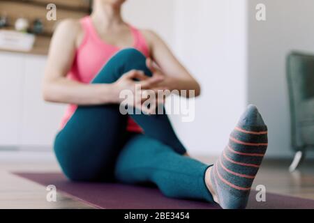 Attraktive Frau, die Yoga zu Hause praktiziert, während sie sich dehnt, in rosa Hemd und blauen Leggings Stockfoto