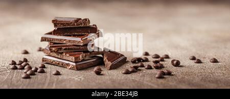 Scheiben von dunkler Schokolade mit Schokoladenchips auf braunem Hintergrund Nahaufnahme. Langes breites Banner Stockfoto