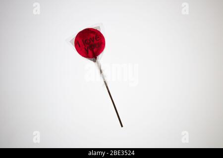 Ein süßes gewickeltes 'I Love You' rotes transparentes Lollypop vor einem hellen weißen Hintergrund, flaches Lay, Draufsicht Stockfoto