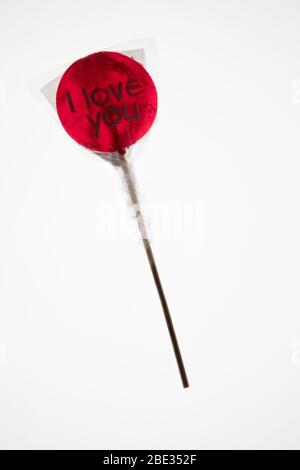 Ein süßes gewickeltes 'I Love You' rotes transparentes Lollypop vor einem hellen weißen Hintergrund, flaches Lay, Draufsicht Stockfoto