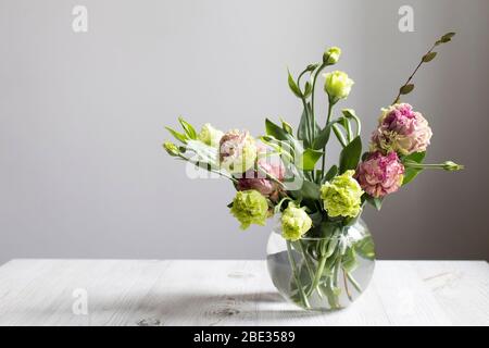 Bouquet von grünen und rosa Terry Lisianthus und Eukalyptus Zweige in einer transparenten runden Vase auf weißem Hintergrund. Brautstrauß Stockfoto