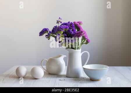 Weiße Steingutkanne mit Limonium, Tassen Tee und ein paar Eiern. Frühstück. Kopierbereich Stockfoto