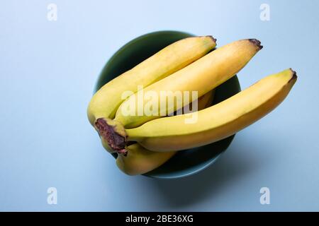 Ein frischer Blick auf einen Haufen Bananen, die in einer hellblauen Schüssel mit einem pastellfarbenen hellblauen Hintergrund ruhen, Draufsicht Stockfoto