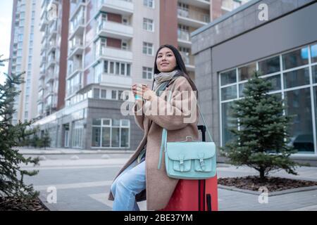 Dunkelhaarige junge Frau in einem beigefarbenen Mantel beim Kaffee Stockfoto