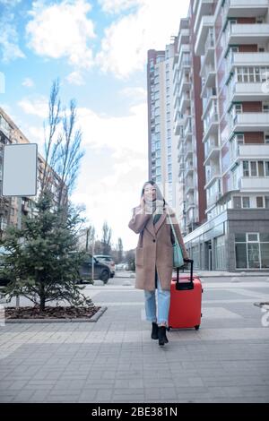 Dunkelhaarige junge Frau in einem beigefarbenen Mantel, die am Telefon spricht Stockfoto