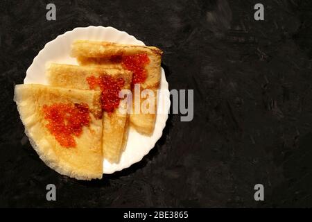 Frische Pfannkuchen mit rotem Kaviar auf dunkelgrauem Hintergrund mit Kopierfläche. Pfannkuchen im russischen Stil für die Pfannkuchen-Woche. Stockfoto