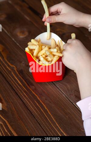 Hände von kleinen Mädchen nehmen Scheiben von salzigen pommes frites. Nur Hände sind im Rahmen, Gesicht ist nicht sichtbar. Seitenansicht. Vertikal. Lieferung von Lebensmitteln, ungesunde ch Stockfoto