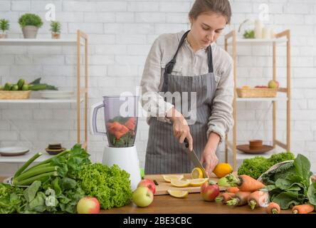 Junge Frau bereitet veganen Smoothie mit Grüns, Zitrusfrüchten Stockfoto