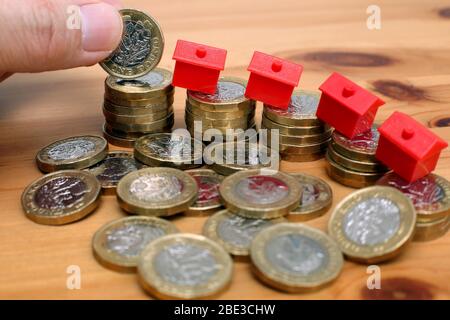 Ein Haufen Pfund-Münzen mit Monopolhäusern, die einen schnellen Rückgang der Immobilienpreise aufgrund der Covid-19 Virus Pandemie andeuten. Stockfoto