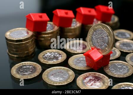 Ein Haufen Pfund-Münzen mit Monopolhäusern, die einen schnellen Rückgang der Immobilienpreise aufgrund der Covid-19 Virus Pandemie andeuten. Stockfoto