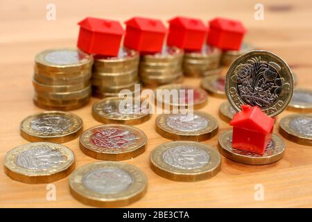 Ein Haufen Pfund-Münzen mit Monopolhäusern, die einen schnellen Rückgang der Immobilienpreise aufgrund der Covid-19 Virus Pandemie andeuten. Stockfoto