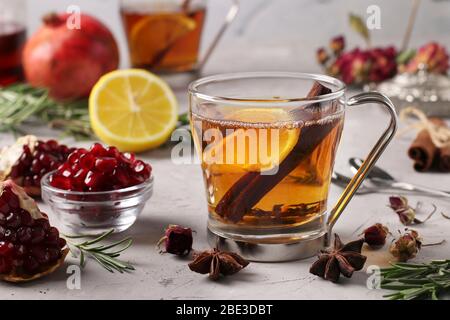 Granatapfel Tee mit Zitrone und Zimt Stick in zwei transparenten Tassen auf grauem Beton Hintergrund, wärmende Wellness-Drink Stockfoto