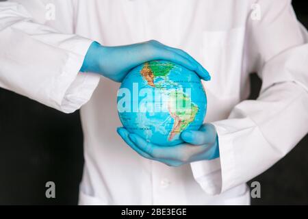 Zugeschnittenes Bild eines männlichen Arztes mit sterilen Gesichtsmaskenhandschuhen aus medizinischem Gown, isoliert auf blauem Hintergrund. Epidemic pandemic coronavirus 2020-ncov sars kovid-19 Grippe-Virus-Konzept. Halten Sie die Welt der Erde fest Stockfoto