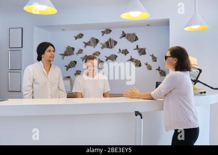 Gast einchecken im Hotel, männlichen und weiblichen Angestellten an der Rezeption sprechen und Gruß Frau Gast Stockfoto