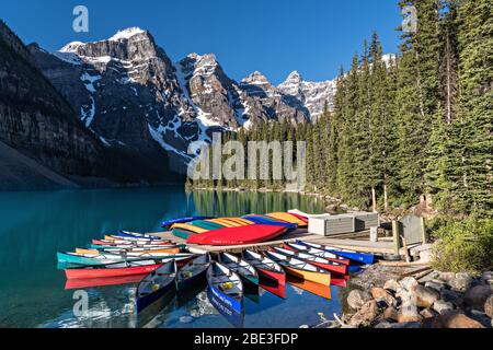 Farbenfrohe Kanus dockten im türkisfarbenen Wasser von Lake Louise und dem schneebedeckten Fairview Mountain dahinter im Banff National Park in Alberta, Kanada. Stockfoto