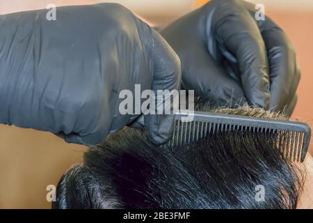 Haarfärbefarbe auf der Kopfhaut von einem Friseur mit schwarzen Gummihandschuhen aufgetragen. Haarfärbestyling zu Hause mit einem Kamm auf den Haarwurzeln. Stockfoto