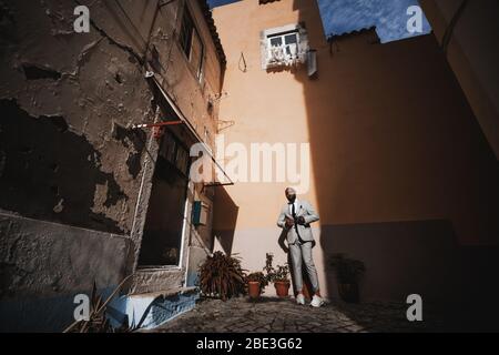 Ein typischer alter portugiesischer Hof mit antiken Häusern, Fenstern und der Veranda, mit einem eleganten bärtigen Afrikaner in einem karierten Kostüm auf dem Stockfoto