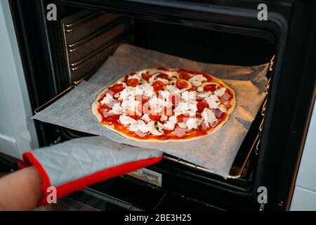 Frauenhände, die eine traditionelle margarita Pizza ins Backen bringen. Zubereitung einer original italienischen Pizza Stockfoto