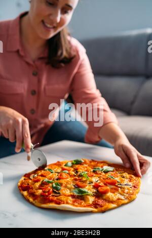 Frau schneidet eine traditionelle italienische margarita Pizza in ihrem Wohnzimmer. Bleiben Sie zu Hause Stockfoto