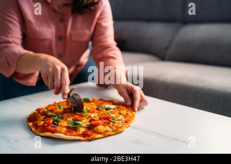 Frau schneidet eine traditionelle italienische margarita Pizza in ihrem Wohnzimmer. Bleiben Sie zu Hause Stockfoto