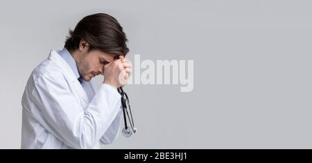 Profil Porträt von depressiven überarbeiteten männlichen Arzt mit Stethoskop in den Händen Stockfoto