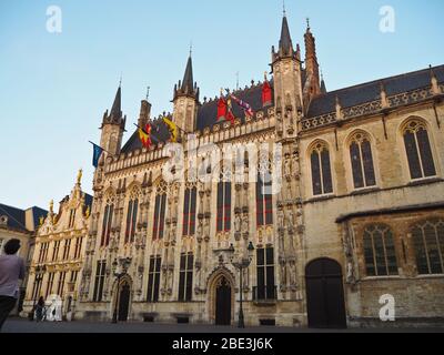 Fassade eines typischen flämischen Gebäudes auf einem öffentlichen Platz in Brügge, Belgien, aus Stein und Ziegeln mit Türmen und Fahnen Stockfoto