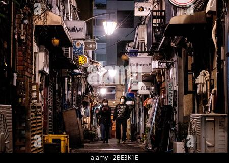 Ein Paar spazierendurch Golden Gai, das berühmte Nachtleben in Shinjuku.die japanische Regierung hat den Ausnahmezustand ausgerufen, um die Präfekturen Tokio, Osaka, Saitama, Kanagawa, Chiba, Hyogo und Fukuoka ab dem 7. April abzudecken und wird bis zum 6. Mai andauern. Tokyos Gouverneur Yuriko Koike hat Restaurants und Bars gebeten, um 20 Uhr geschlossen zu werden, da sich der COVID-2019-Virus ausbreitet. Stockfoto