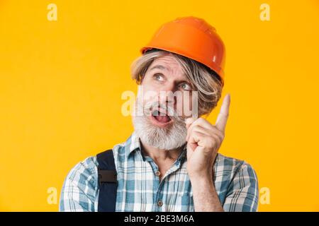 Foto von älteren grauhaarigen bärtigen Mann Baumeister im Helm posiert isoliert über gelben Wand Hintergrund haben eine Idee. Stockfoto