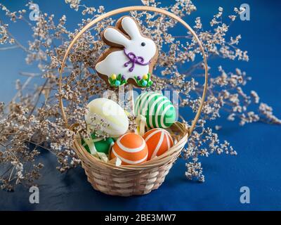 Bunte Ostereier und Lebkuchen in Form eines Hasen mit einem Weidenkorb. Christlicher Frühling Stockfoto