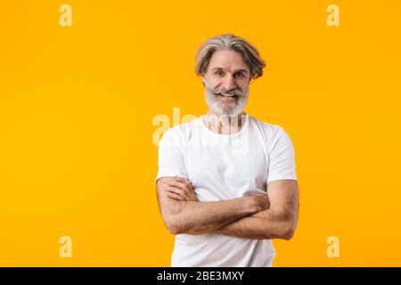 Bild von fröhlichen positiven älteren grauhaarigen bärtigen Mann posiert isoliert über gelben Wand Hintergrund. Stockfoto