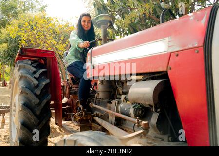 Junge indische Mädchen auf einem roten Traktor mit riesigen Rädern und Motor ausgesetzt Stockfoto