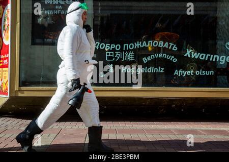Moskau, Russland.11. April 2020. Ein Arbeiter in Spezialkleidung machen Desinfektion auf Arbat Straße in Moskau während der neuartigen Coronavirus COVID-19 Pandemie in Russland. Ein Arbeiter läuft vor dem Hintergrund einer Vitrine mit Inschriften in verschiedenen Sprachen und liest "Willkommen" Stockfoto