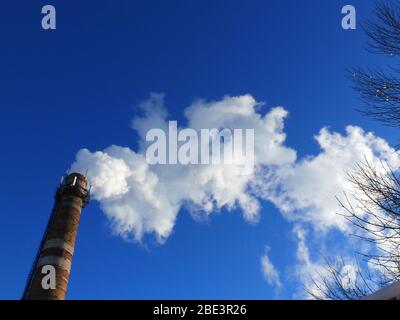 Rohre einer alten Fabrik werfen Wolken von giftigem weißem Rauch in den Himmel, die die Atmosphäre schädigen. Urbaner Smog aus Rauch aus Kesselhäusern. Weißer Rauch aus einem Kamin gegen einen blauen klaren Himmel. Stockfoto