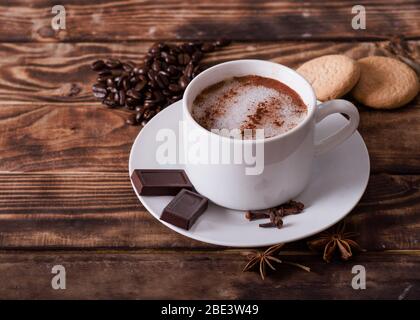 Kaffe mit Schaum, Kuchen, herzförmige Kaffeebohnen auf dem Holztisch. Flach lag ohne Leute Stockfoto