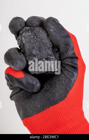 Braunkohle in der Hand gehalten. Material zum Heizen von Häusern auf einem Arbeitshandschuh. Heller Hintergrund. Stockfoto