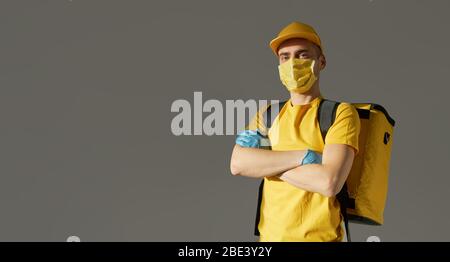 Sichere Lieferung von Lebensmitteln. Kurier in gelber Uniform, Schutzmaske und Handschuhe liefert während der Coronovirus-Quarantäne Essen zum Mitnehmen. Platz für Text kopieren Stockfoto