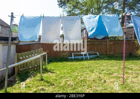 Bettwäsche und Bettwäsche werden frisch gewaschen und hängen an einer Wäscheleine im Garten hinter dem Haus zum Trocknen aus. Stockfoto