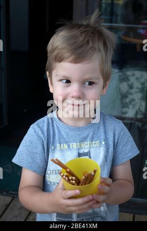 Entzückter junger Junge, der einen Snack, eine Tasse Brezeln hält. Zawady Gmina Rzeczyca Polen Stockfoto