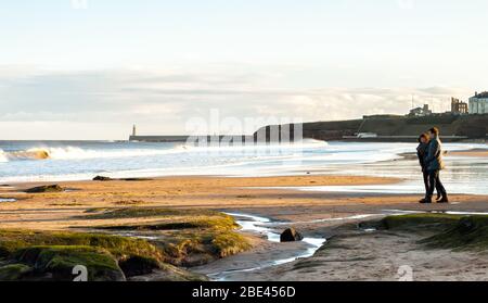 Panoramablick auf Paare, die an der britischen Küste bei Sonnenuntergang in Tynemouth, Großbritannien, spazieren gehen Stockfoto