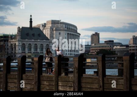 Ein Paar spricht in der Abenddämmerung an einem Pier am South Bank of London, England, Großbritannien, an einem Sommerabend entlang der Themse. Stockfoto