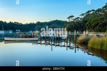 Traditionelle Holzboote liegen an einem Holzsteg am Macquarie Harbour, im Hintergrund liegt die Stadt Strahan über der Bucht. Stockfoto