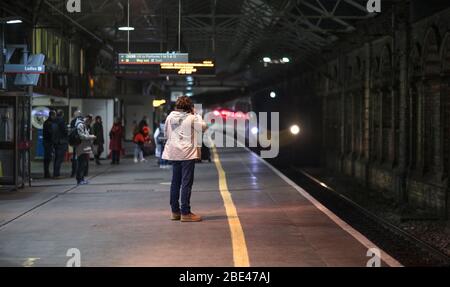Passagiere am Bahnsteig 11 des Bahnhofs Crewe mit den Scheinwerfern eines nachts ankommenden Virgin-Zuges Stockfoto