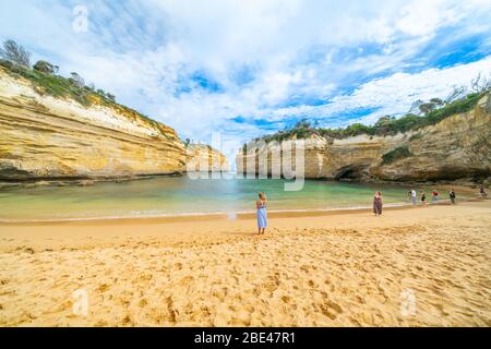 Victoria Australien - März 17 2020; Touristen in der geschützten Bucht in Loch ARD Gorge, umgeben von hohen Kalksteinwänden und Wasser, das über den Strand spült. Stockfoto