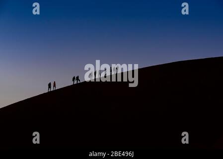 Silhouette von Touristen, die in der Dämmerung Dune 45 besteigen, Sossusvlei, Namib Desert; Namibia Stockfoto